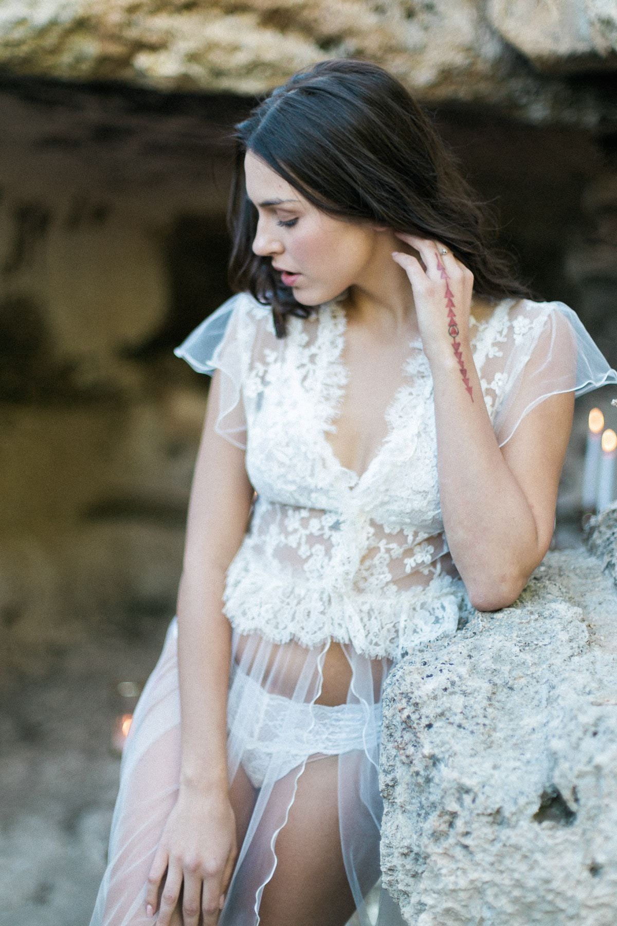 A woman in lingerie and a wedding dress is sitting on a rock.