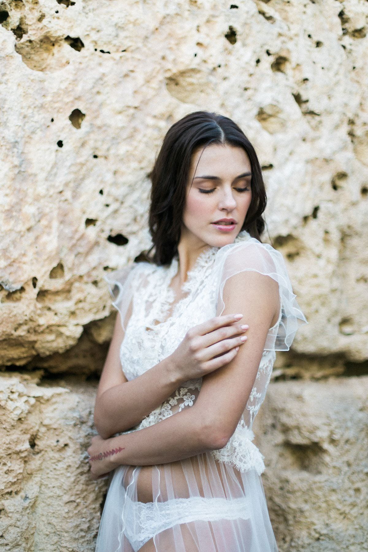 A woman in a white dress and underwear is standing in front of a rock wall.