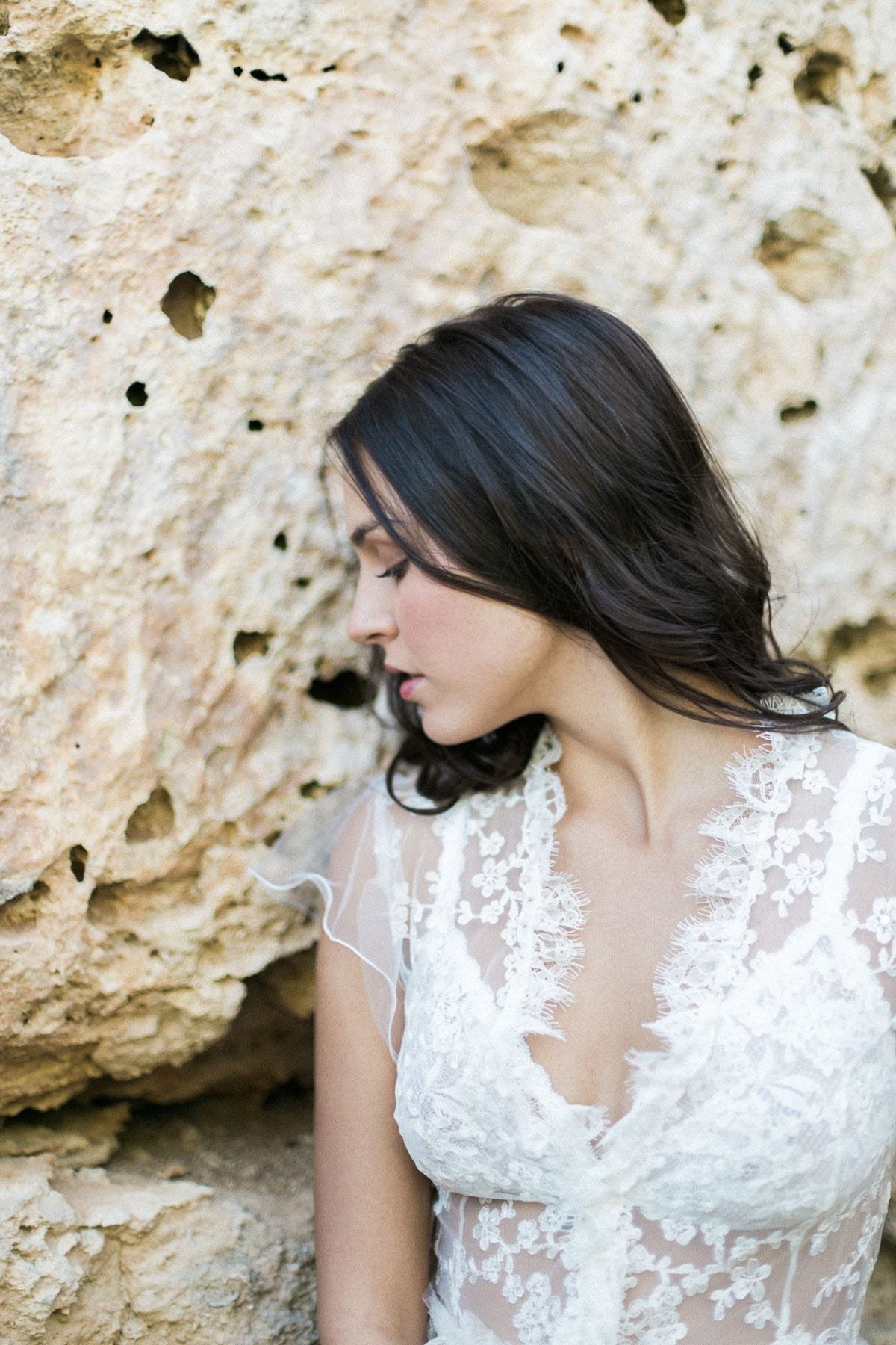 A woman in a white lace dress is sitting on a rock.