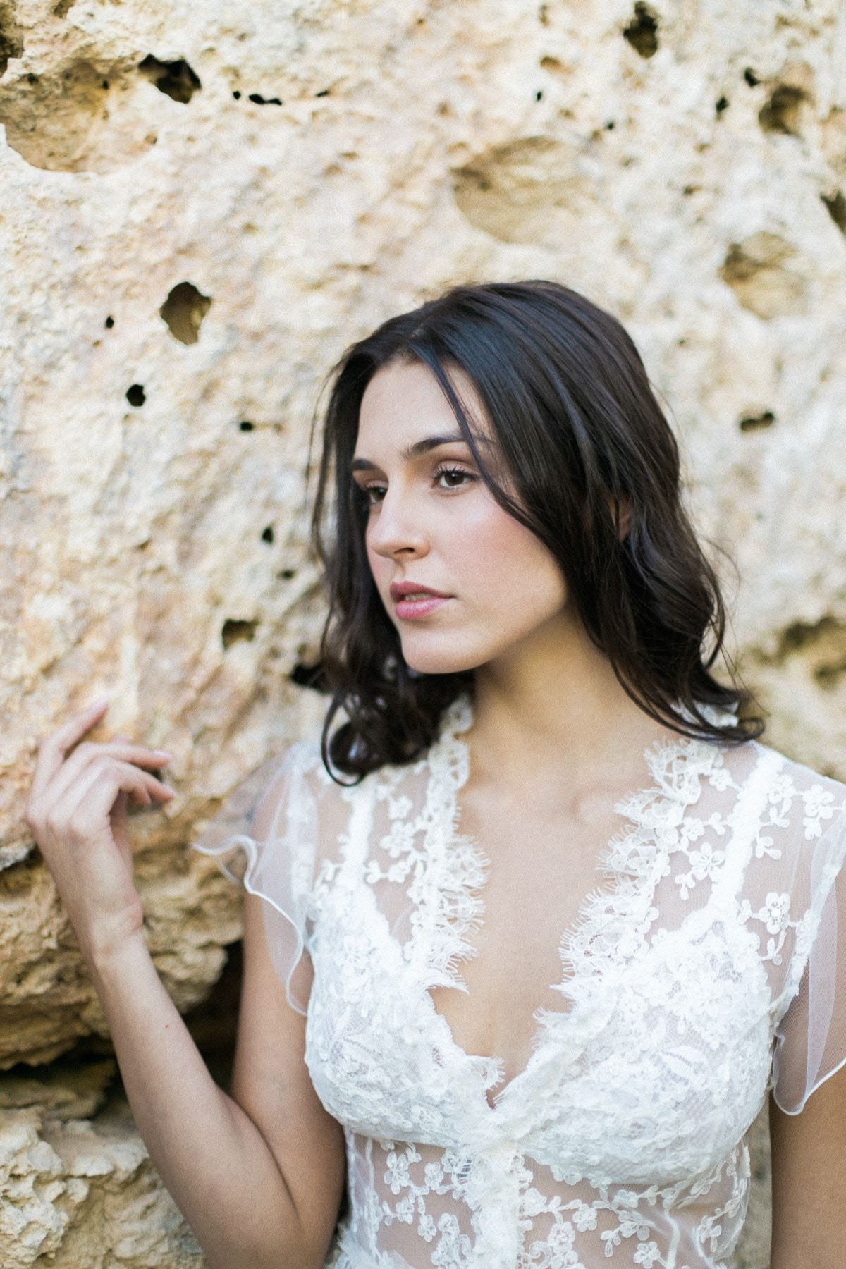 A woman in a white lace dress is standing next to a rock.