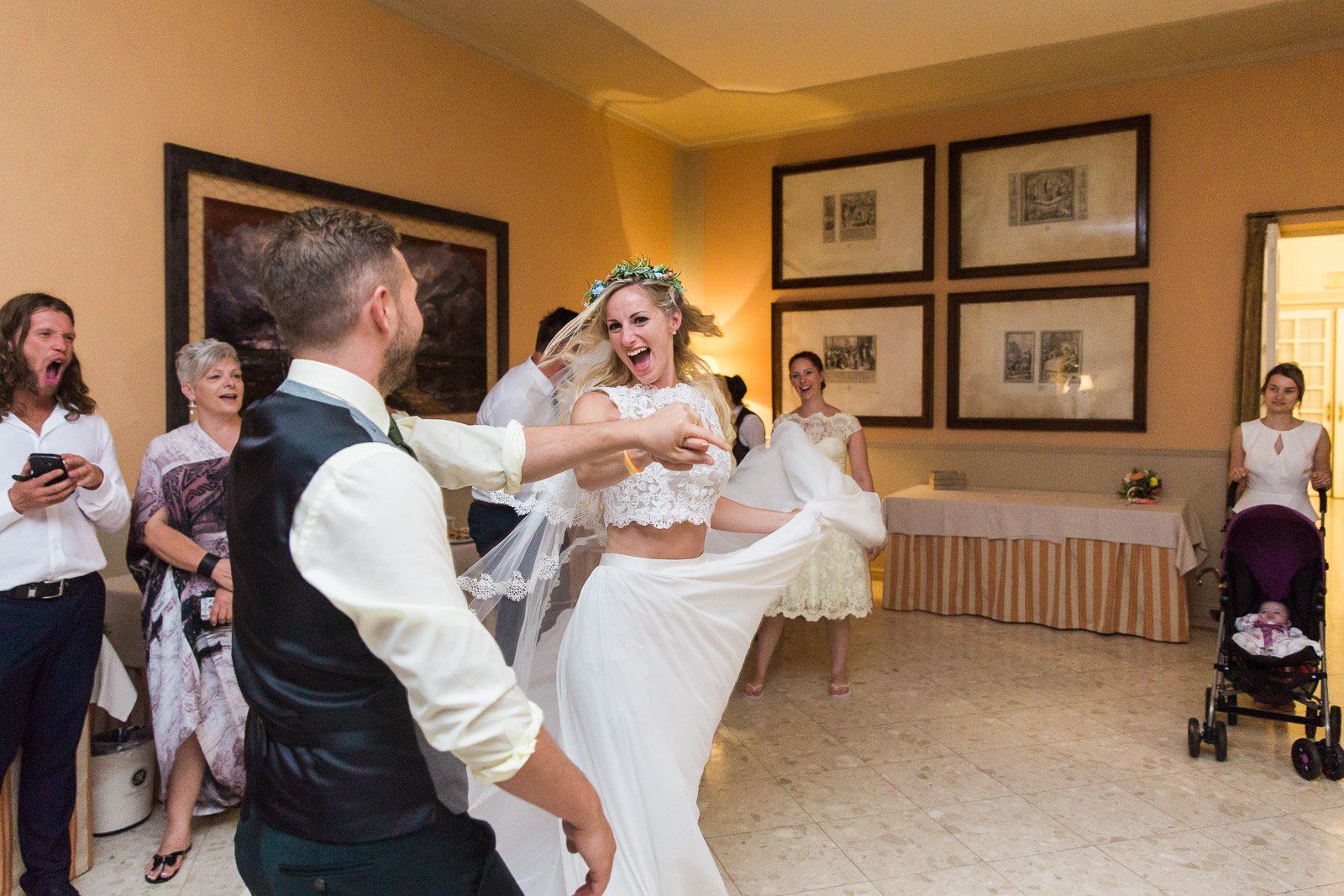 A bride and groom are dancing in a room with their wedding guests.