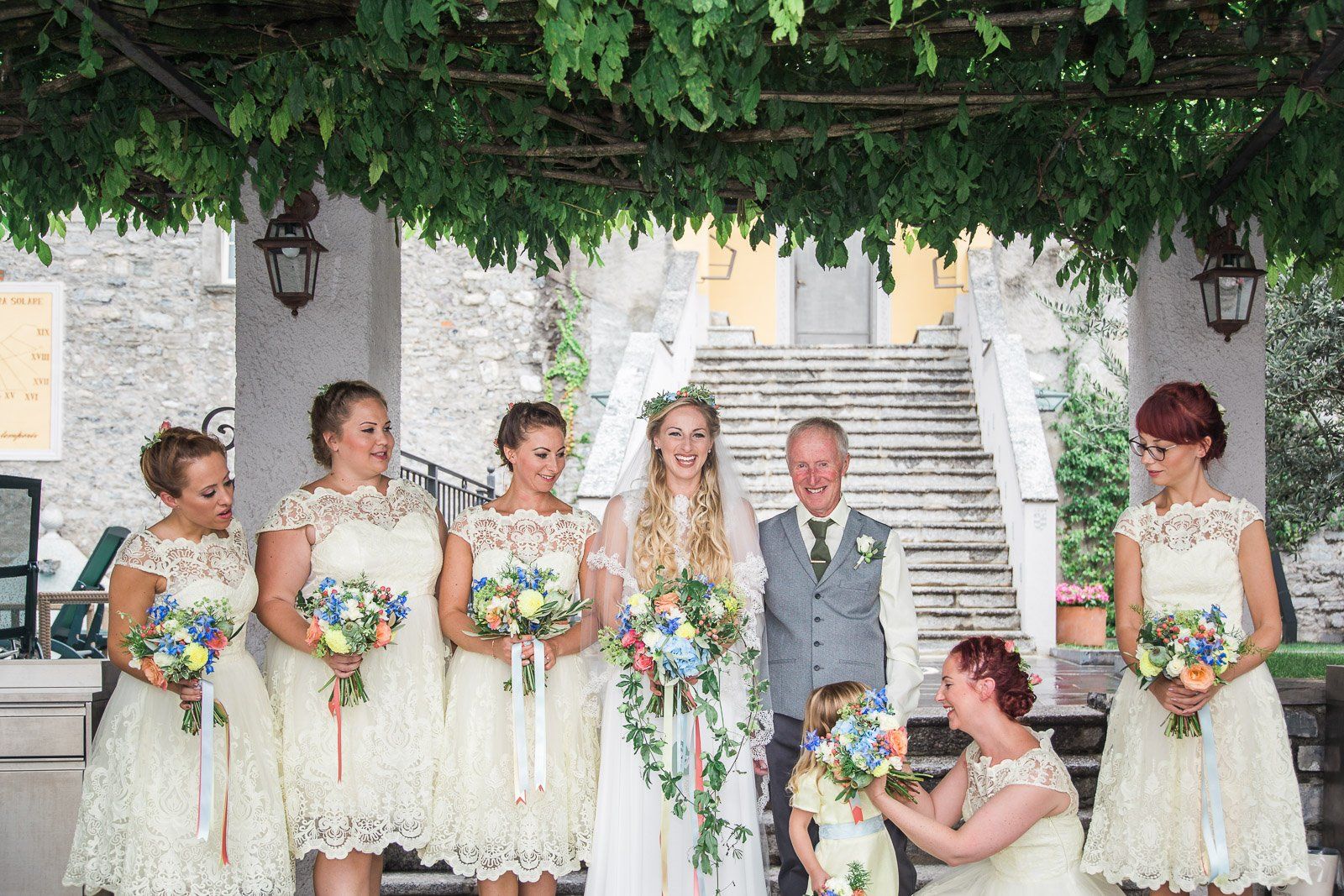 The bride and groom are posing for a picture with their bridesmaids and flower girl.