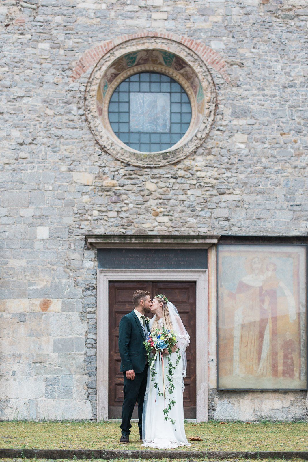 A bride and groom are kissing in front of a church.