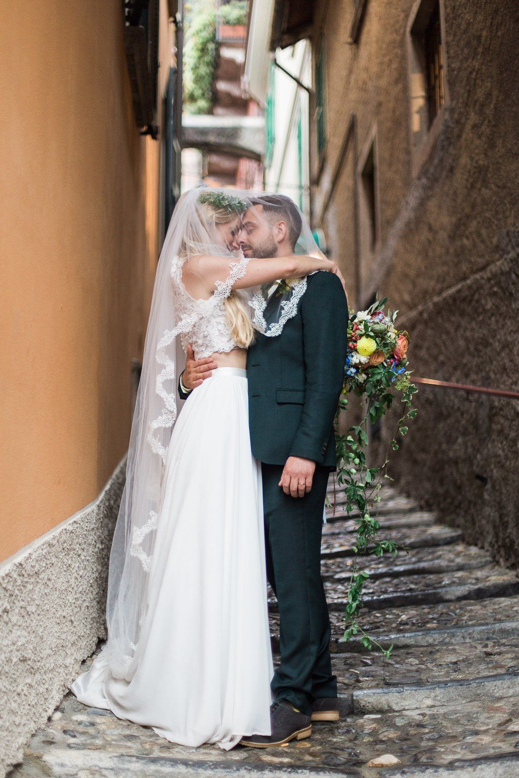A bride and groom are kissing in a narrow alleyway.