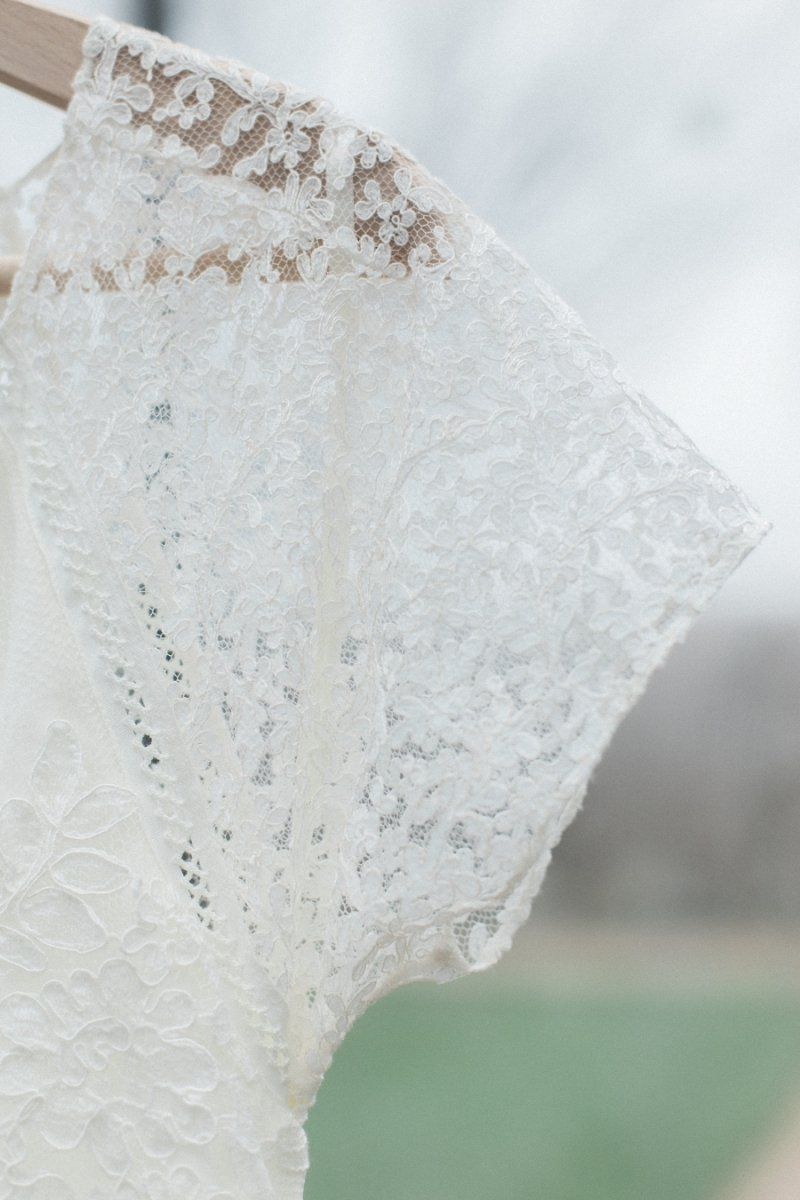 A white lace dress is hanging on a wooden hanger.