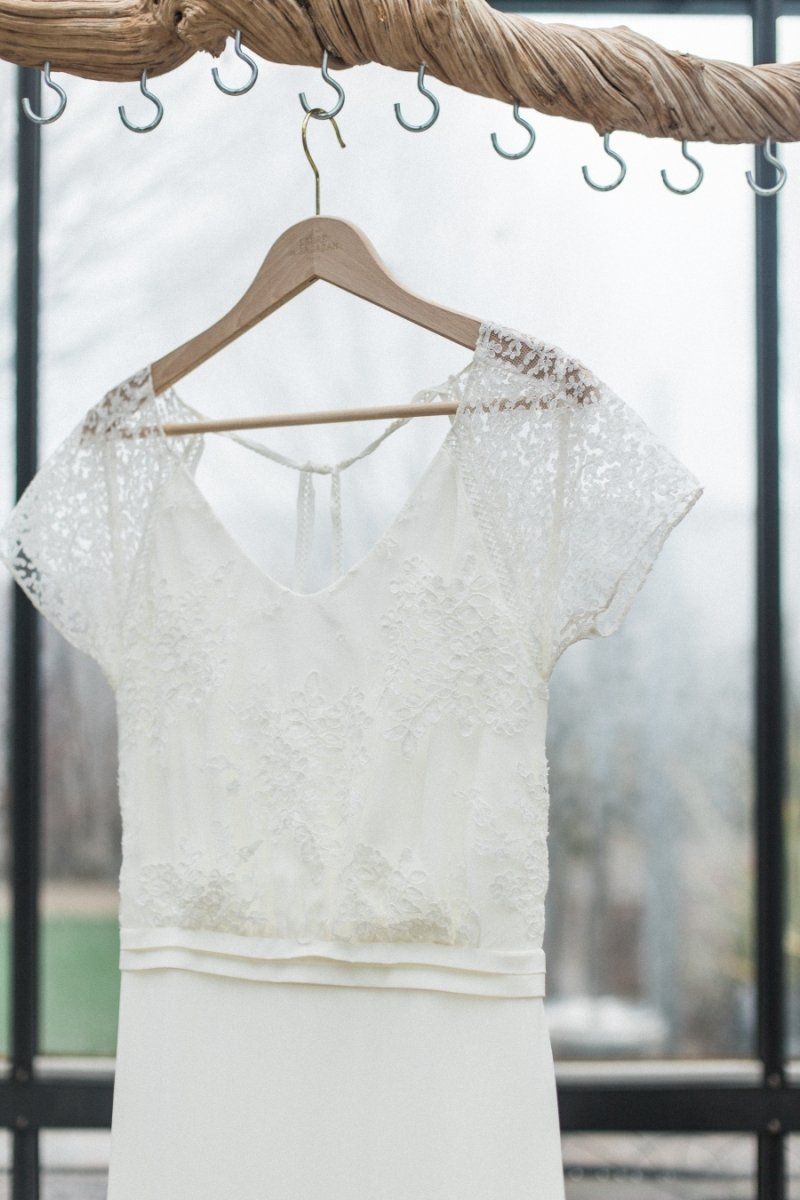 A white lace wedding dress is hanging on a wooden hanger.