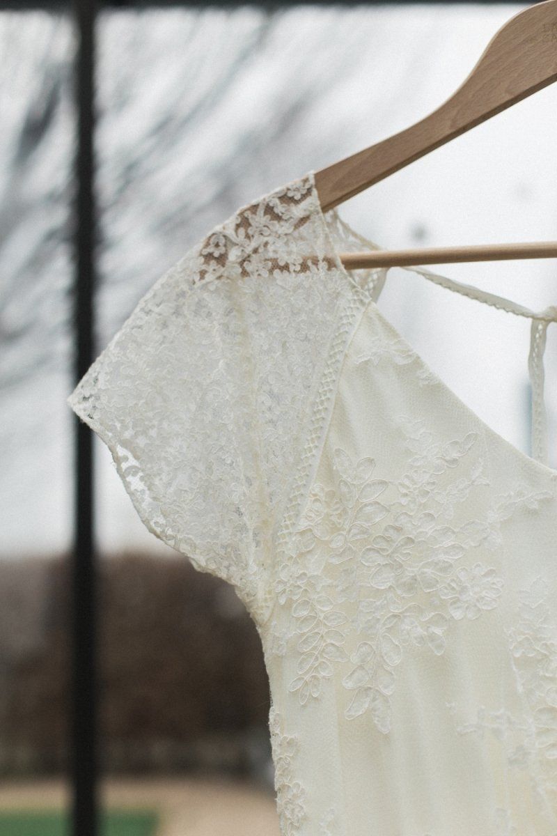 A white lace dress is hanging on a wooden hanger.