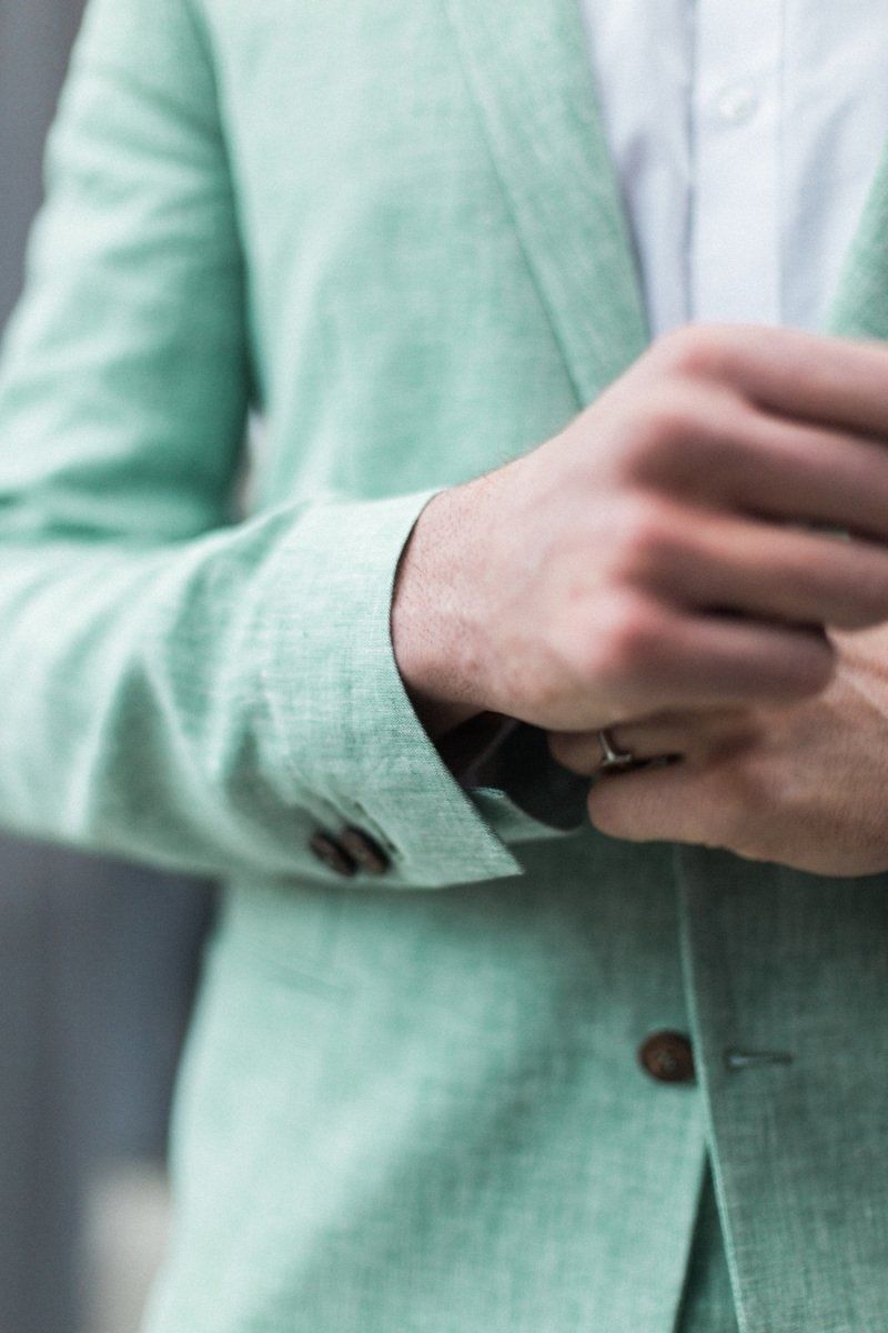 A man in a green suit is adjusting his watch.