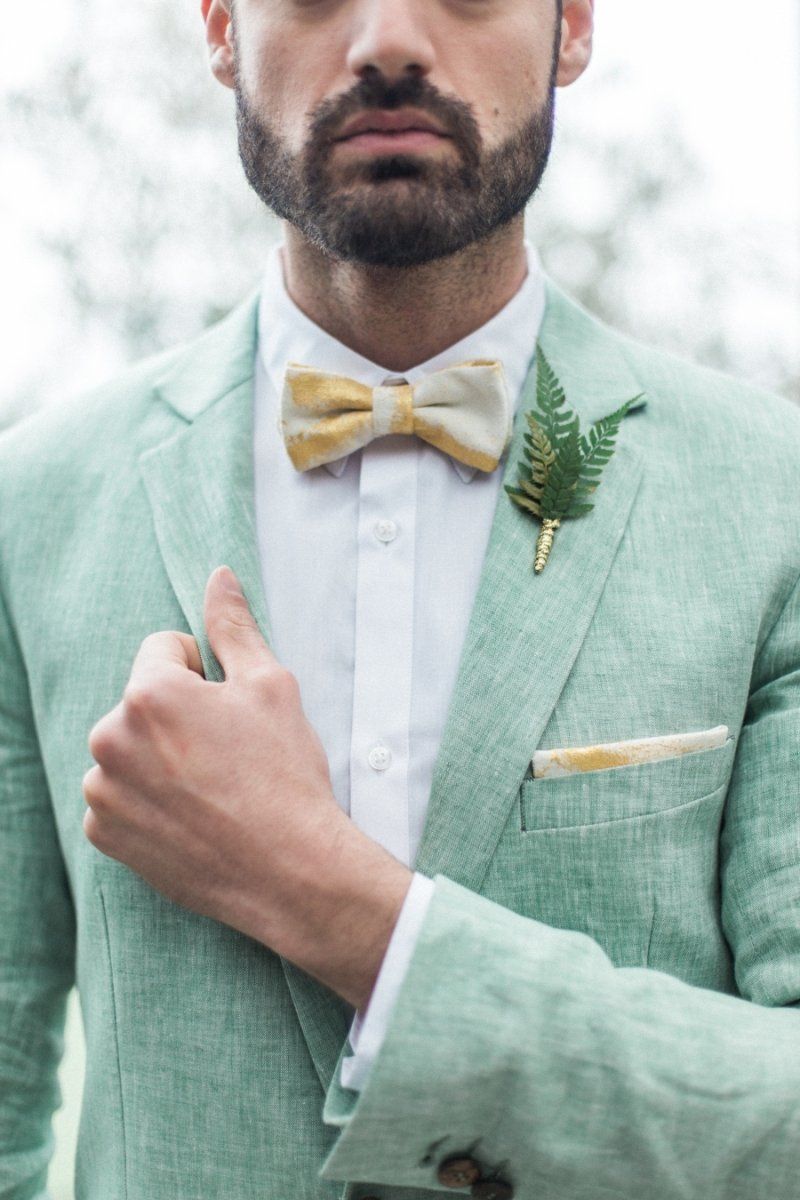 A man with a beard is wearing a green suit and a yellow bow tie.