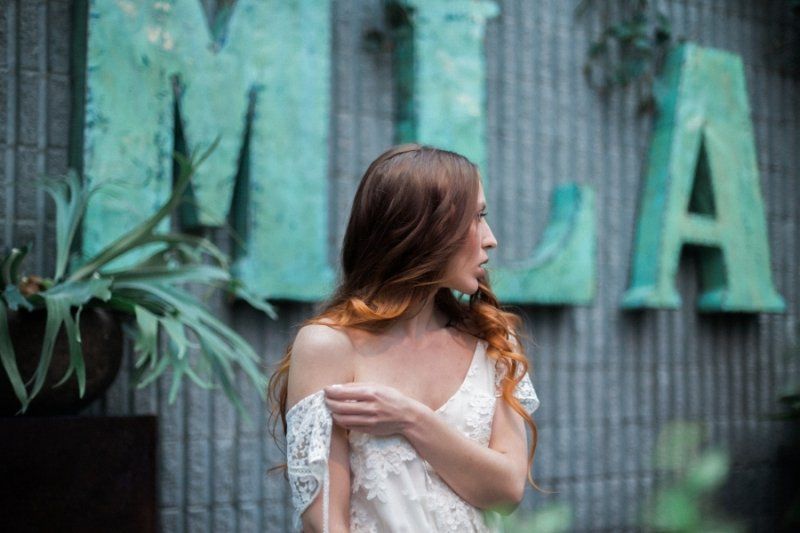 A woman in a white dress is standing in front of a green sign.