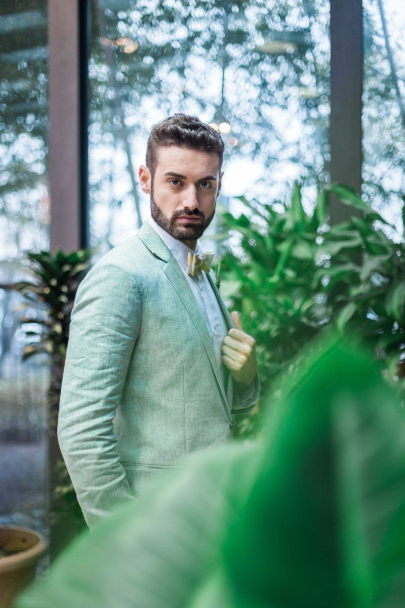A man in a green suit and bow tie is standing in front of a window.