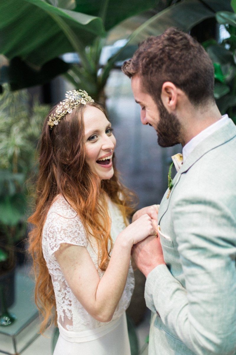 A bride and groom are holding hands and smiling in a greenhouse.