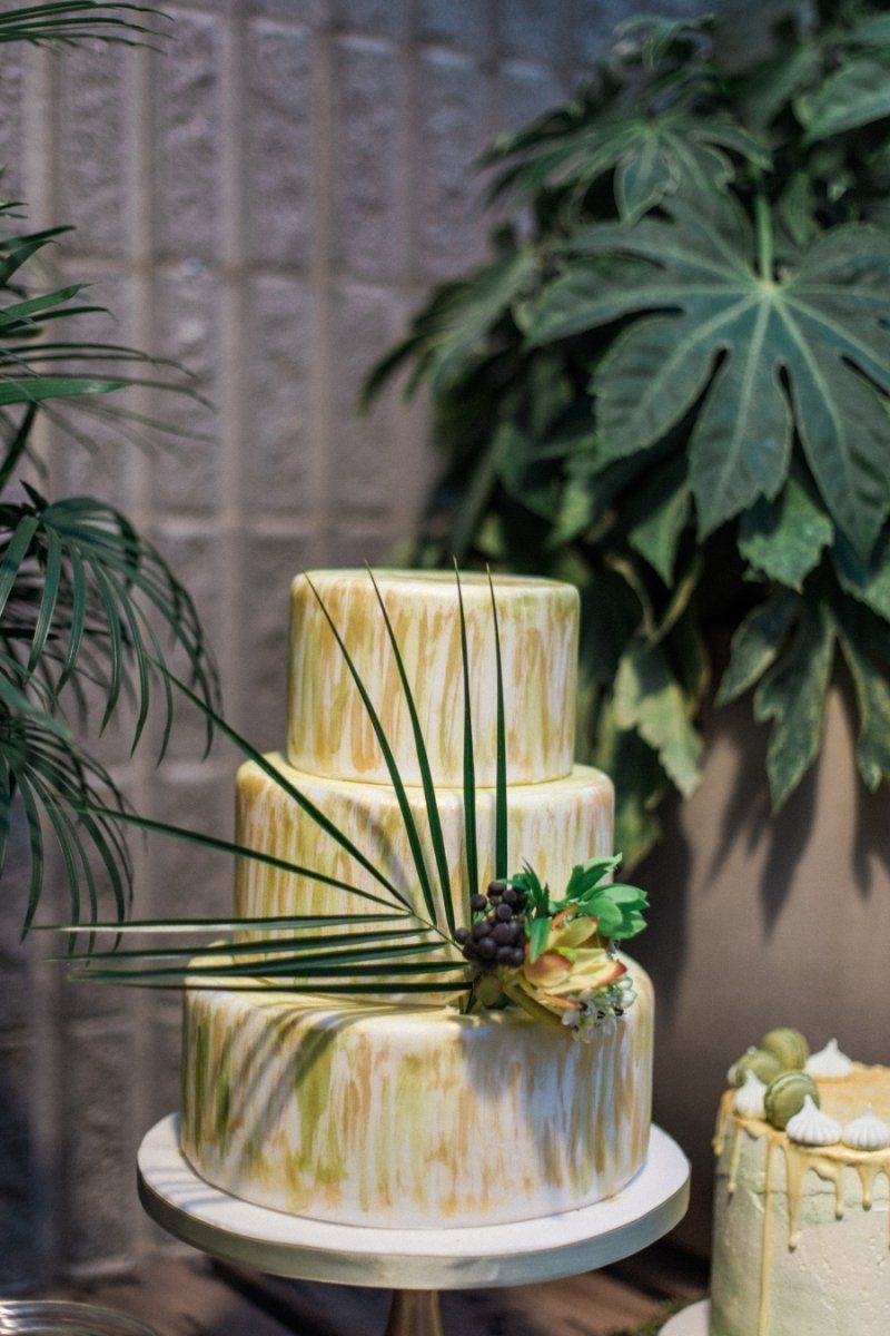 A wedding cake is sitting on top of a cake stand next to a plant.