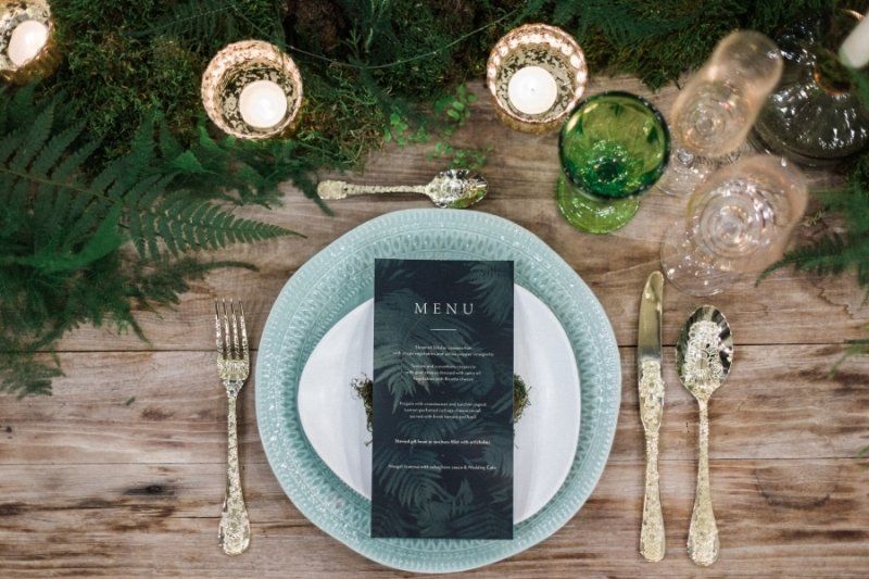 A wooden table topped with plates , silverware , candles and a menu.