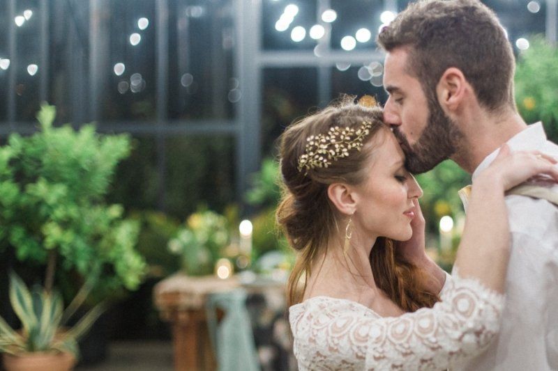 A bride and groom are kissing in a greenhouse.