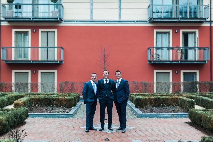 Three men in suits are standing in front of a red building.