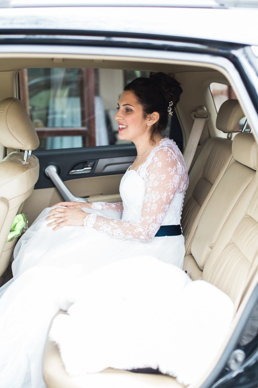 A bride in a wedding dress is sitting in the back seat of a car.