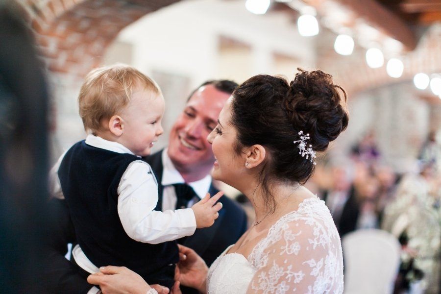 A bride and groom are holding a baby at their wedding reception.
