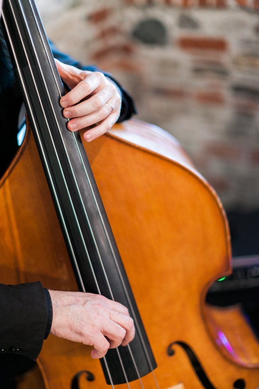 A person is playing a double bass in front of a brick wall.