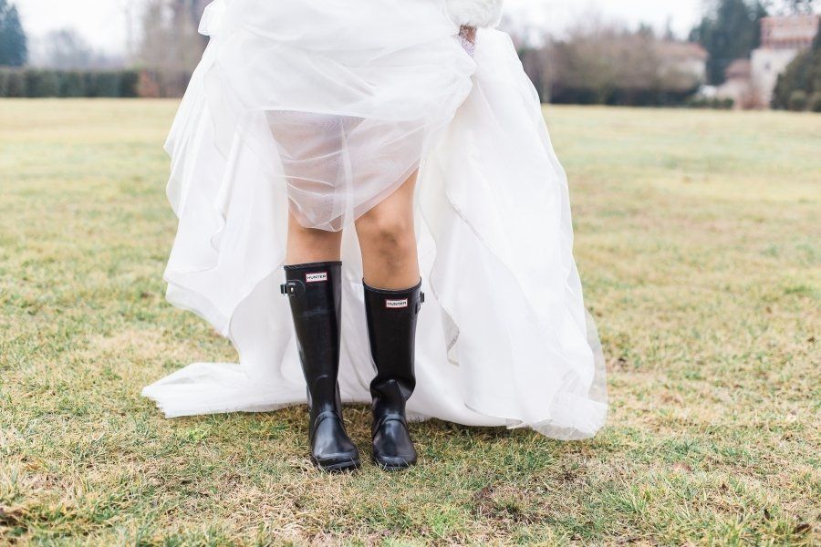 A bride in a white dress and black rain boots is standing in a field.