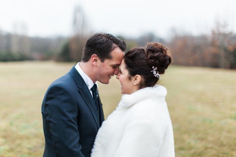 A bride and groom are touching their foreheads in a field.