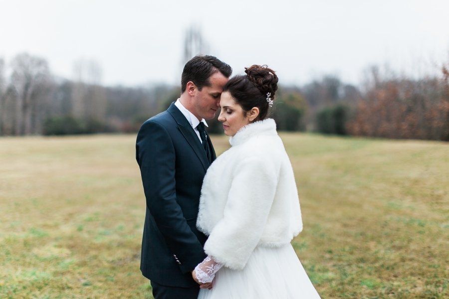 A bride and groom are posing for a picture in a field . the bride is wearing a fur coat.