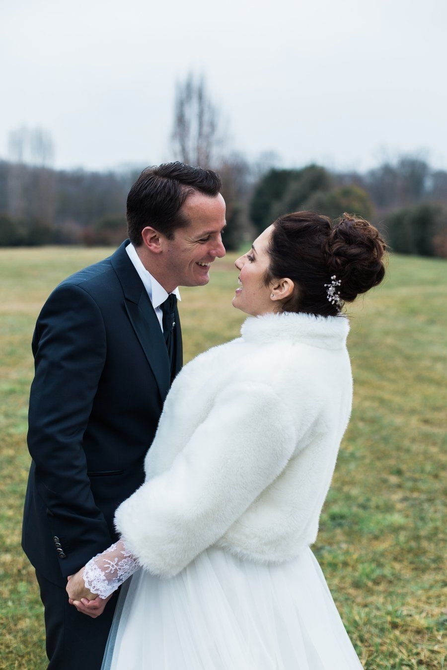 A bride and groom are standing in a field looking at each other.