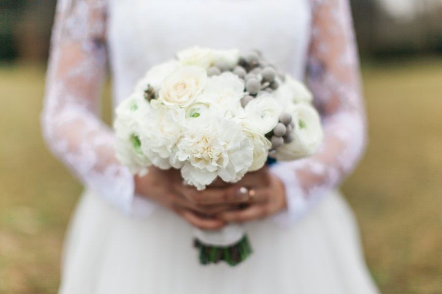 A bride in a white dress is holding a bouquet of white flowers.