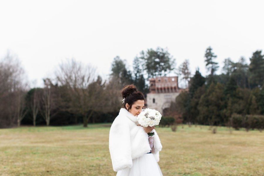 A bride in a white fur coat is holding a bouquet of flowers in a field.