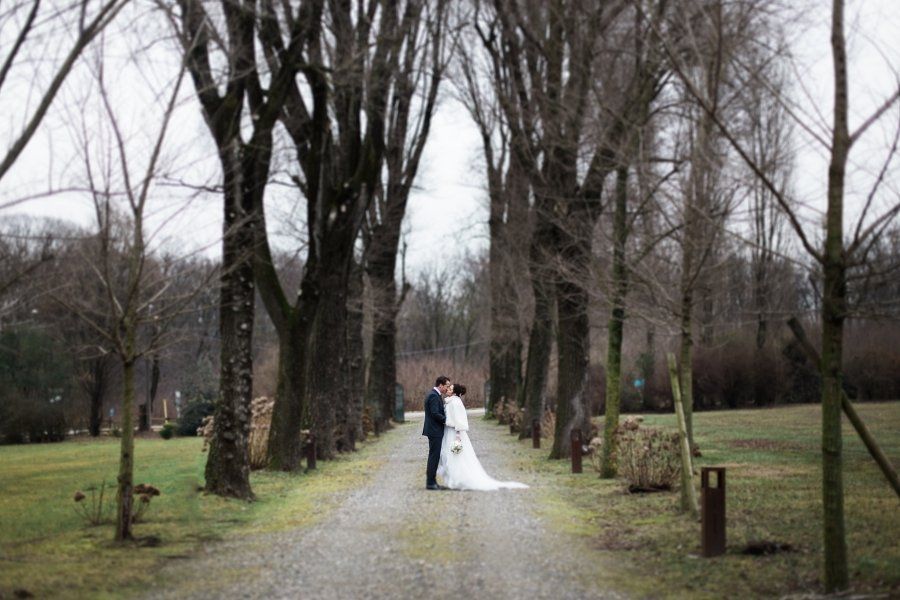 A bride and groom are standing next to each other on a path lined with trees.
