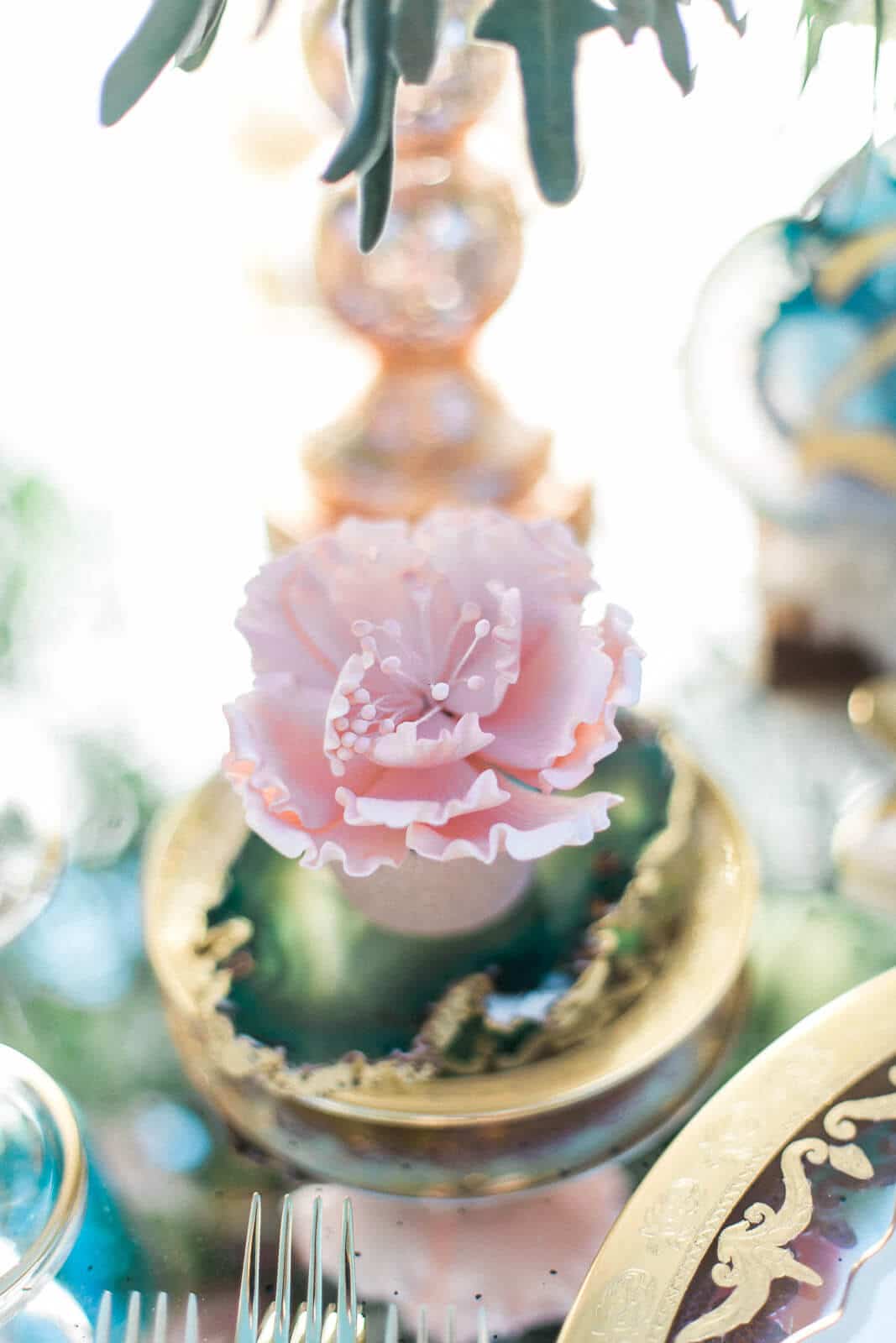A pink flower is sitting on top of a gold plate on a table.