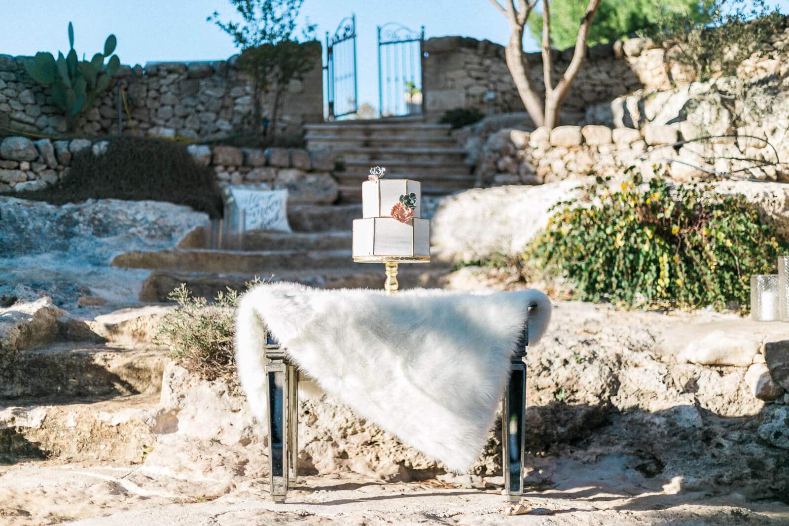 A wedding cake is sitting on top of a table in front of a stone wall.