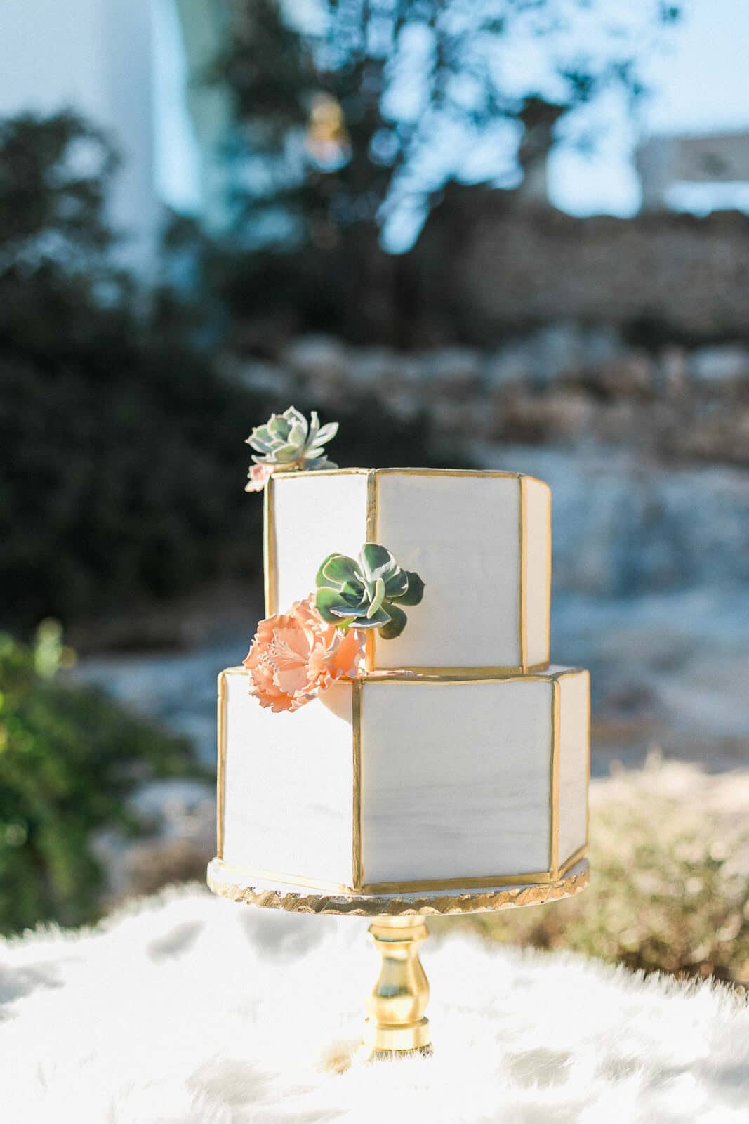 A white and gold wedding cake is sitting on top of a gold cake stand.