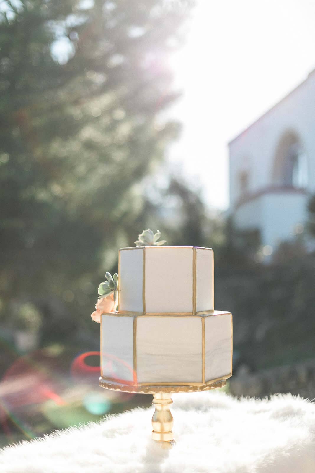 A white and gold wedding cake is sitting on top of a white table.