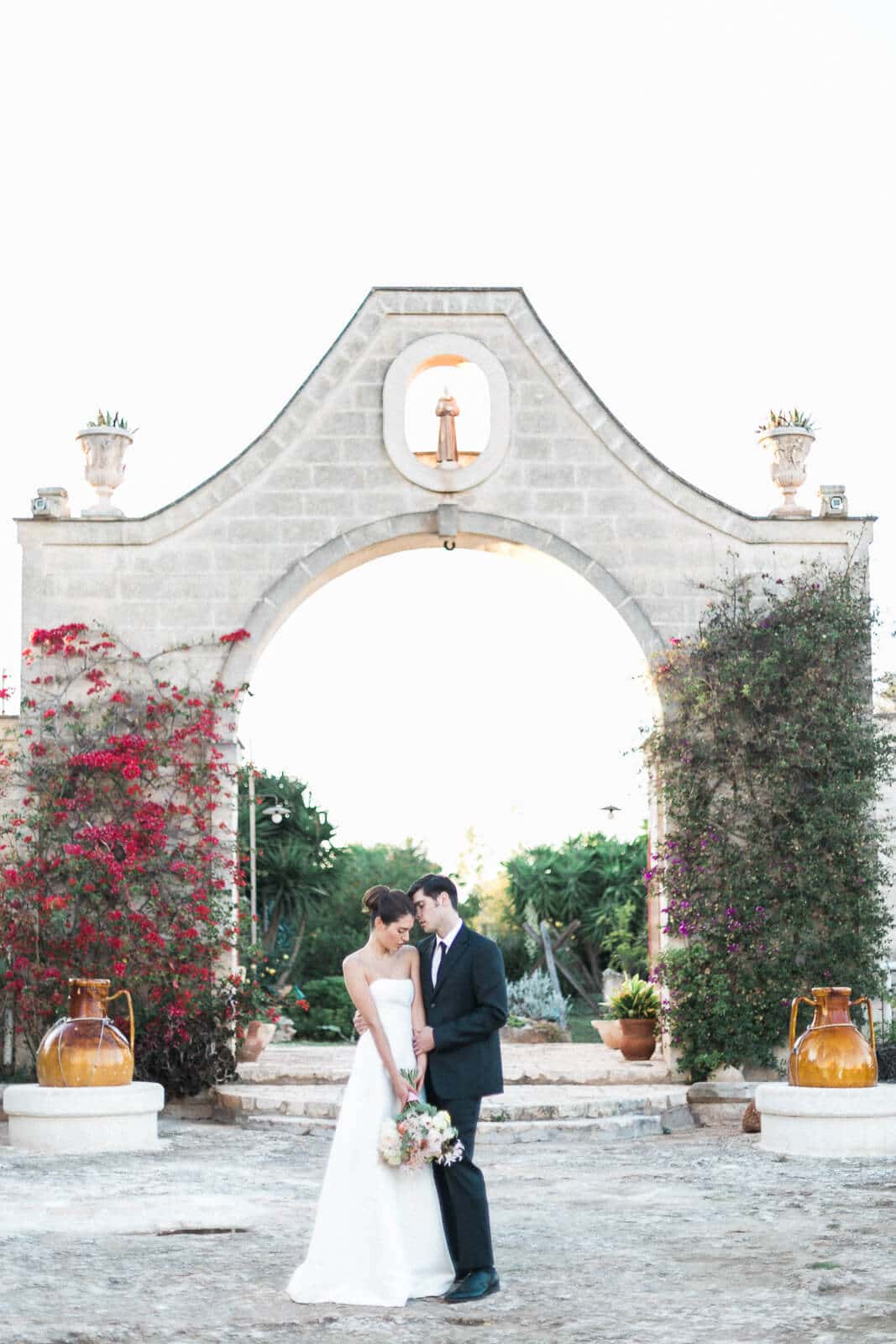 A bride and groom are posing for a picture in front of a stone archway.