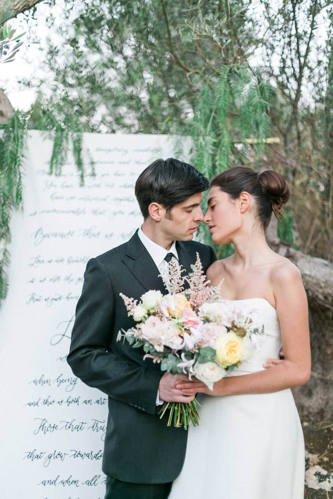 A bride and groom are kissing in front of a large piece of paper.
