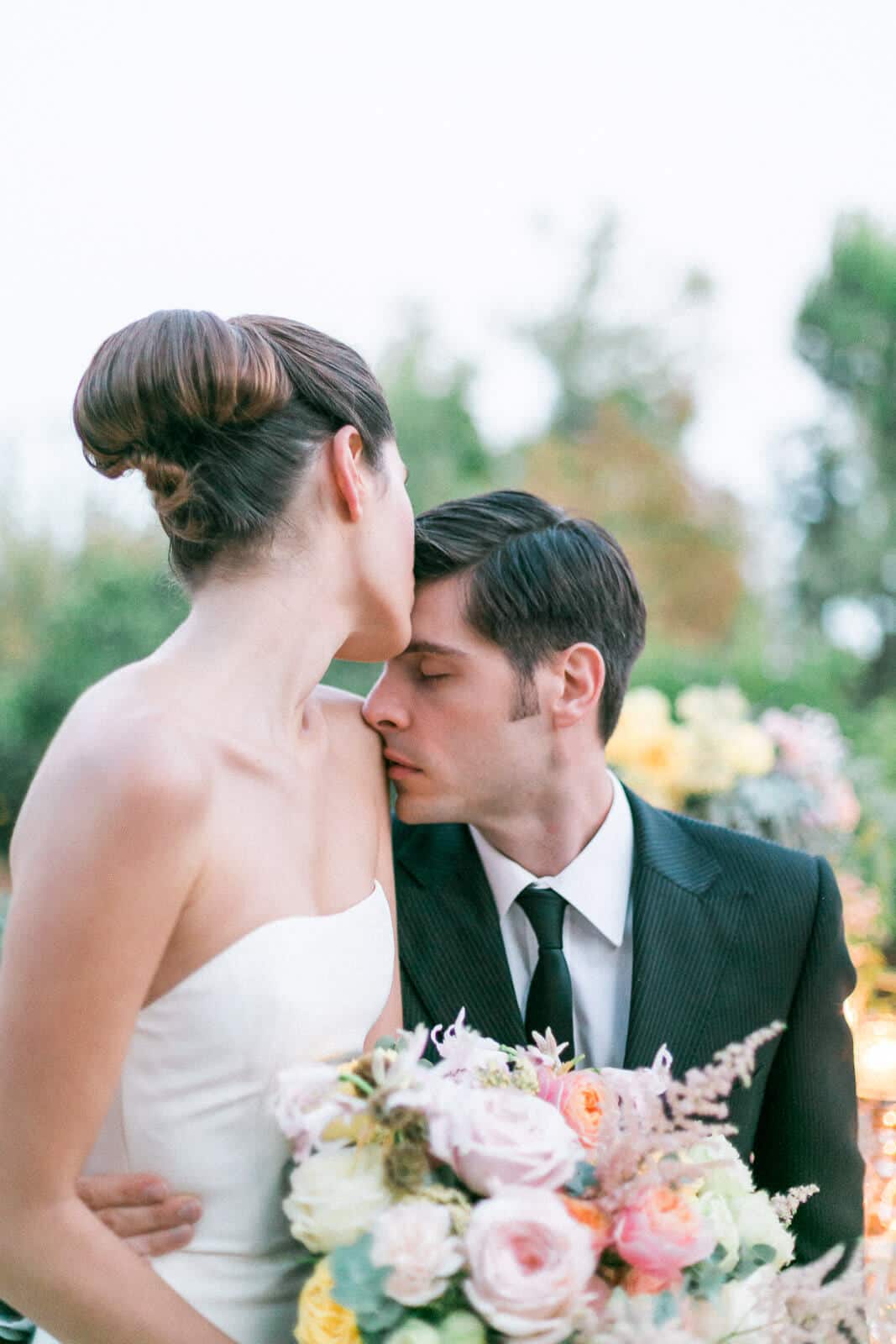A bride and groom kissing while holding a bouquet of flowers.