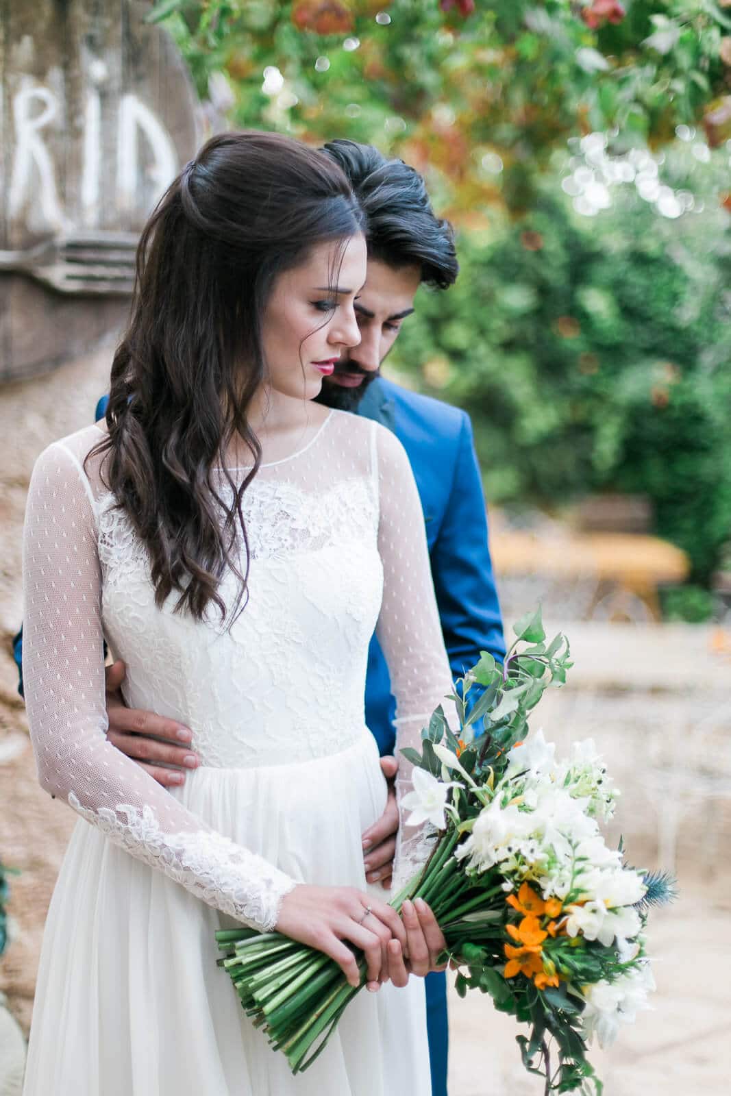 A bride and groom are posing for a picture while the bride is holding a bouquet of flowers.