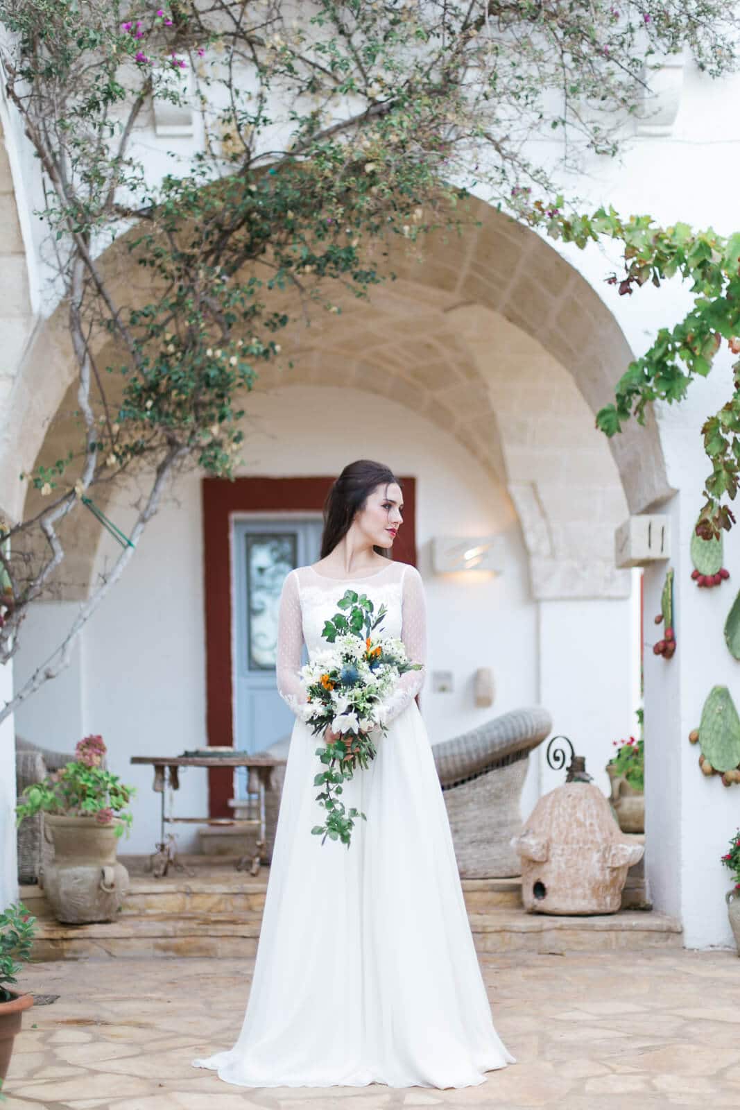 A woman in a wedding dress is standing in front of a building holding a bouquet of flowers.