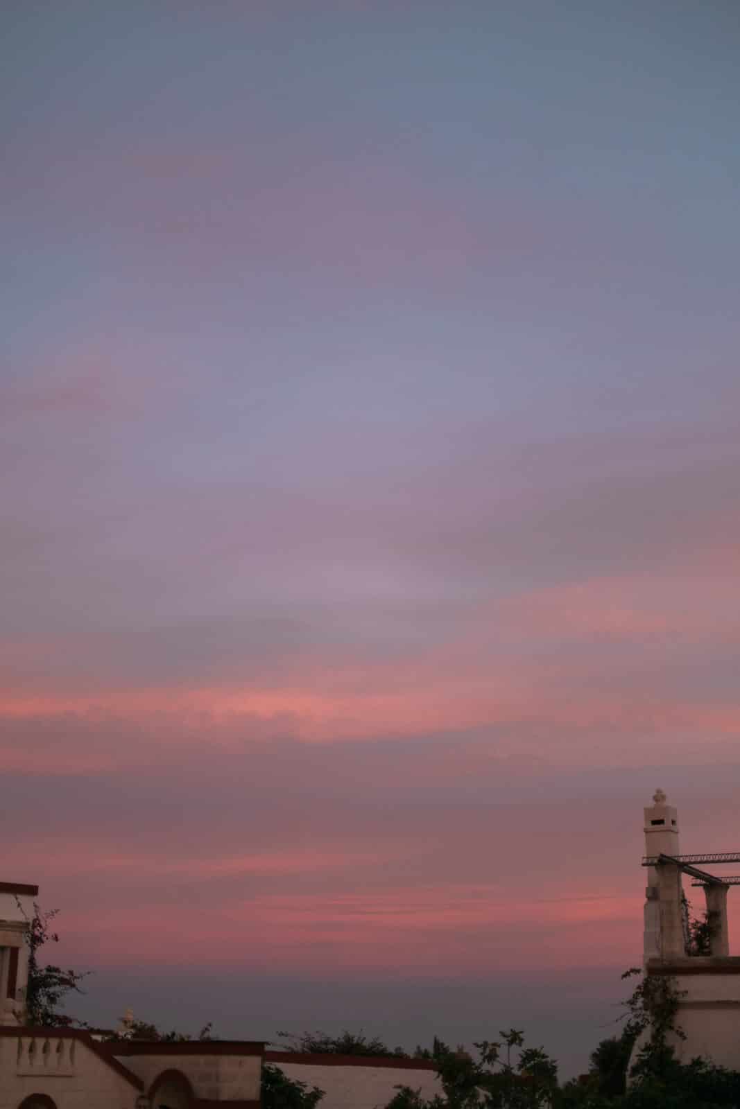 A sunset over a building with a pink sky in the background.