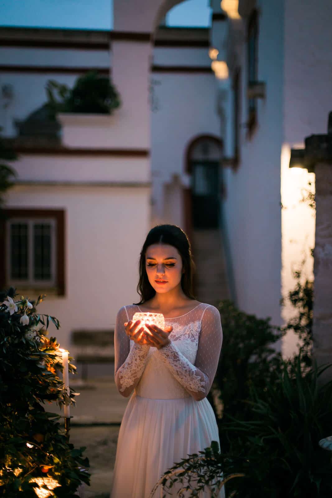 A woman in a white dress is holding a candle in her hands.