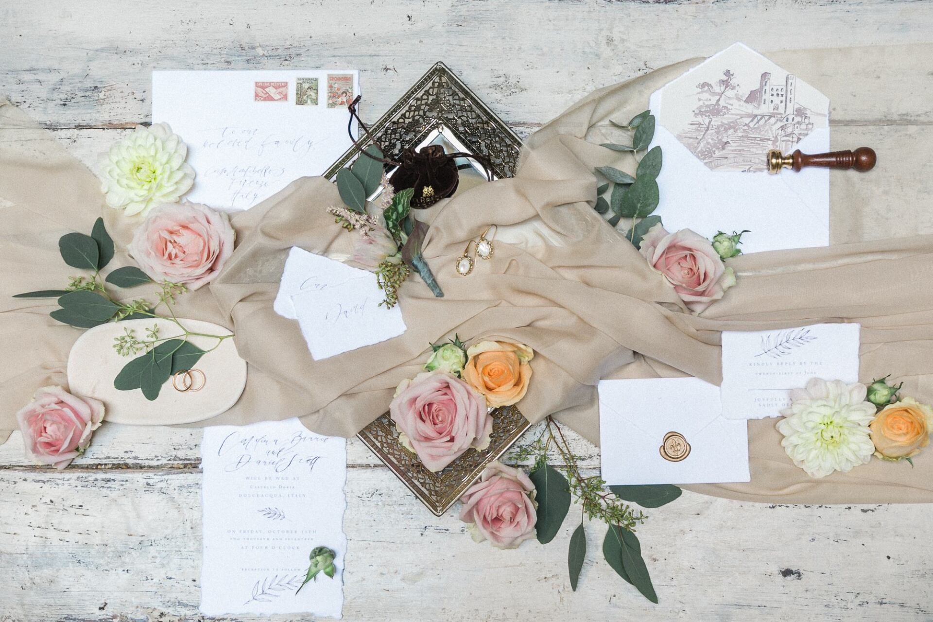 A table topped with invitations , envelopes , flowers and a picture frame.