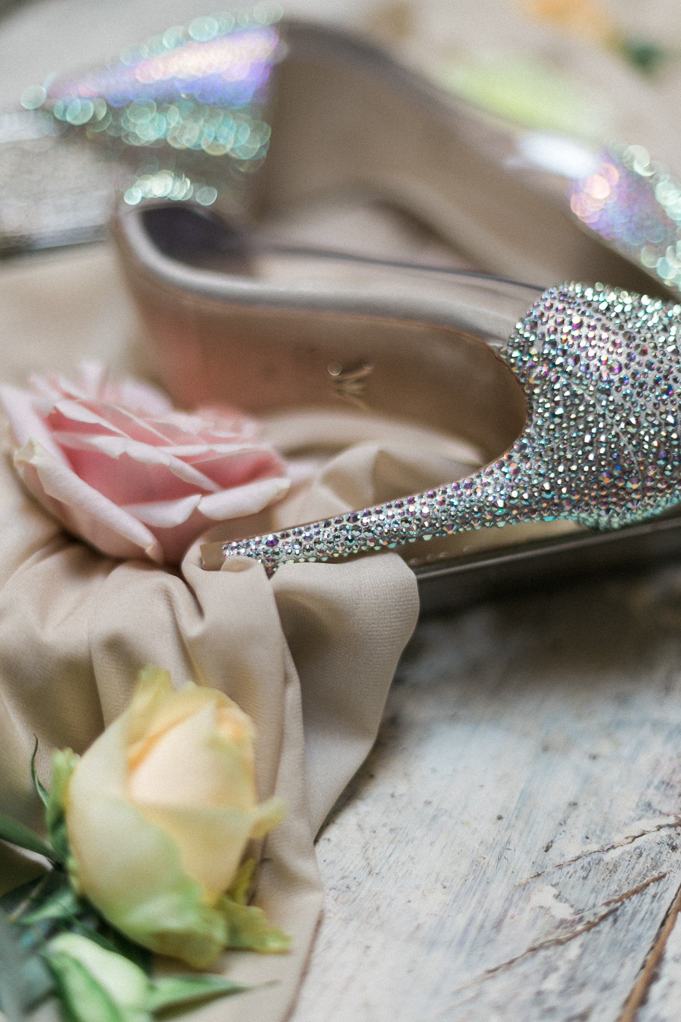 A pair of wedding shoes sitting on top of a wooden table next to a rose.
