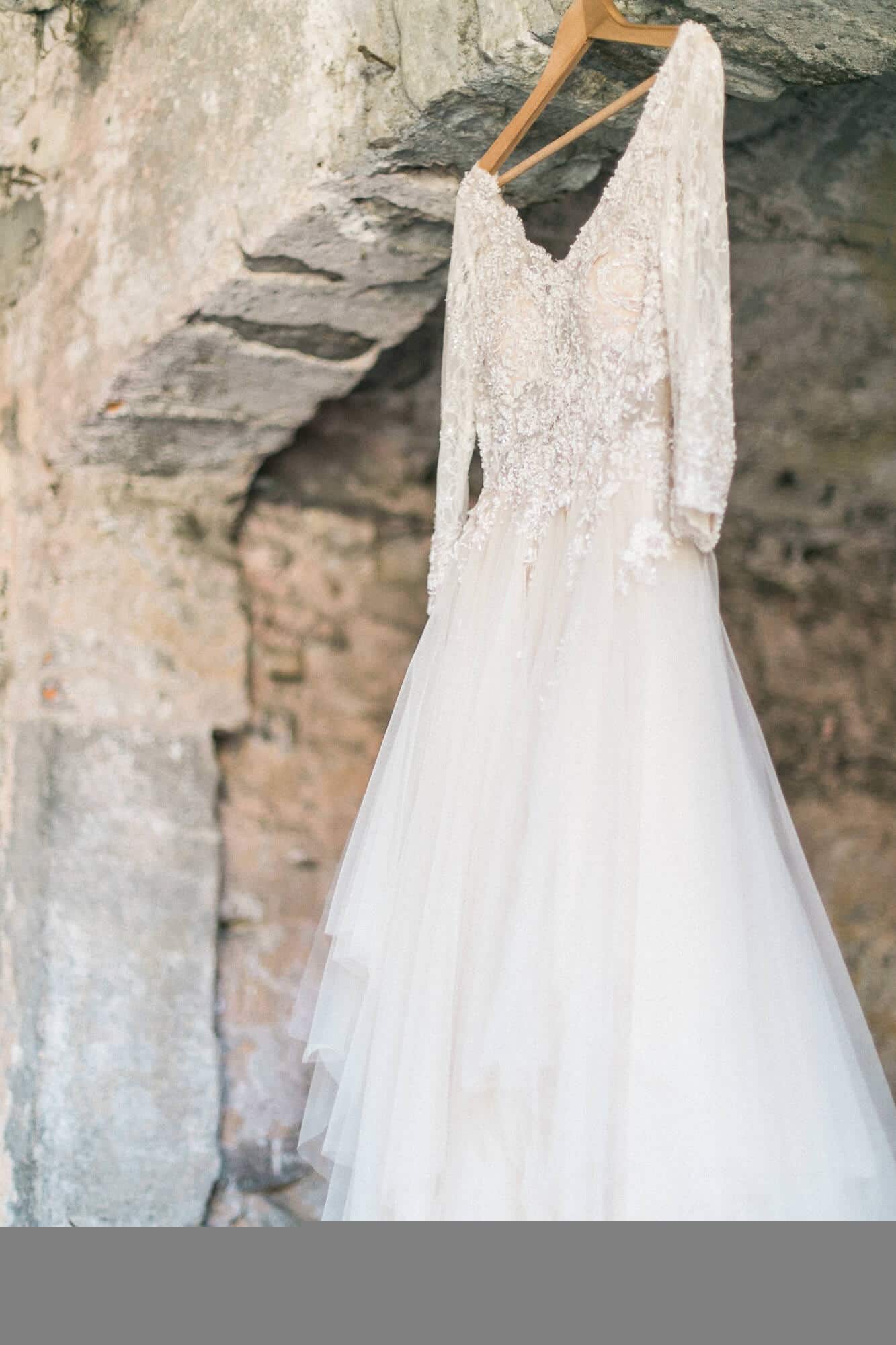 A wedding dress with long sleeves is hanging on a wooden hanger.