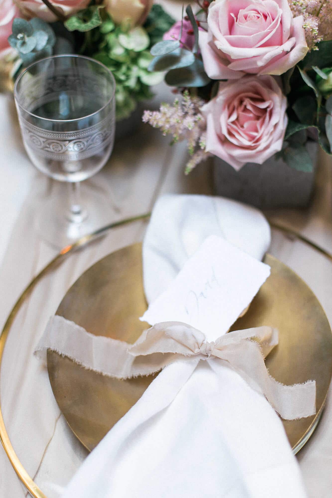 A place setting with a napkin tied with a bow and a glass of wine.