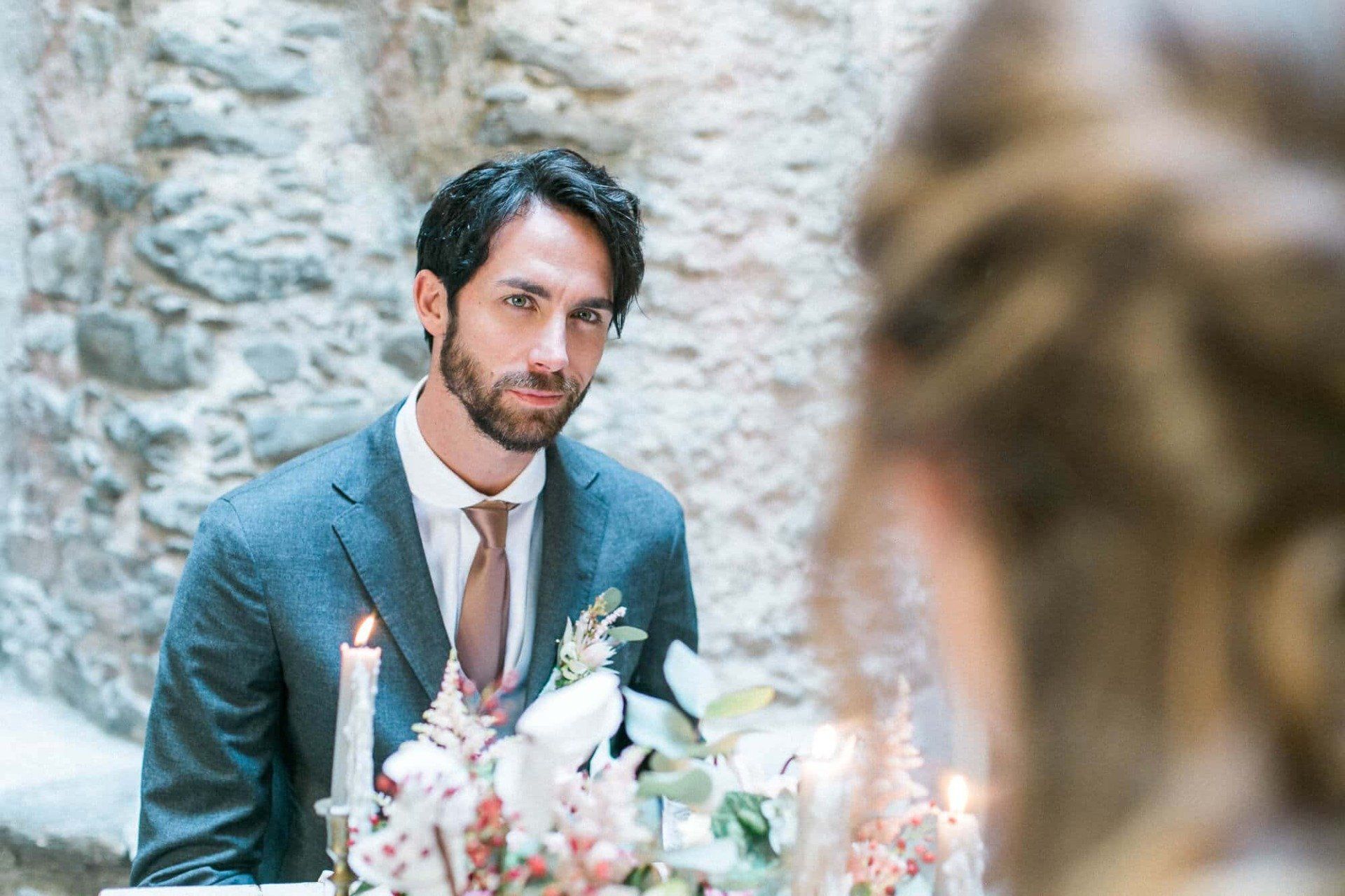 A man in a suit and tie is sitting at a table with flowers and candles.