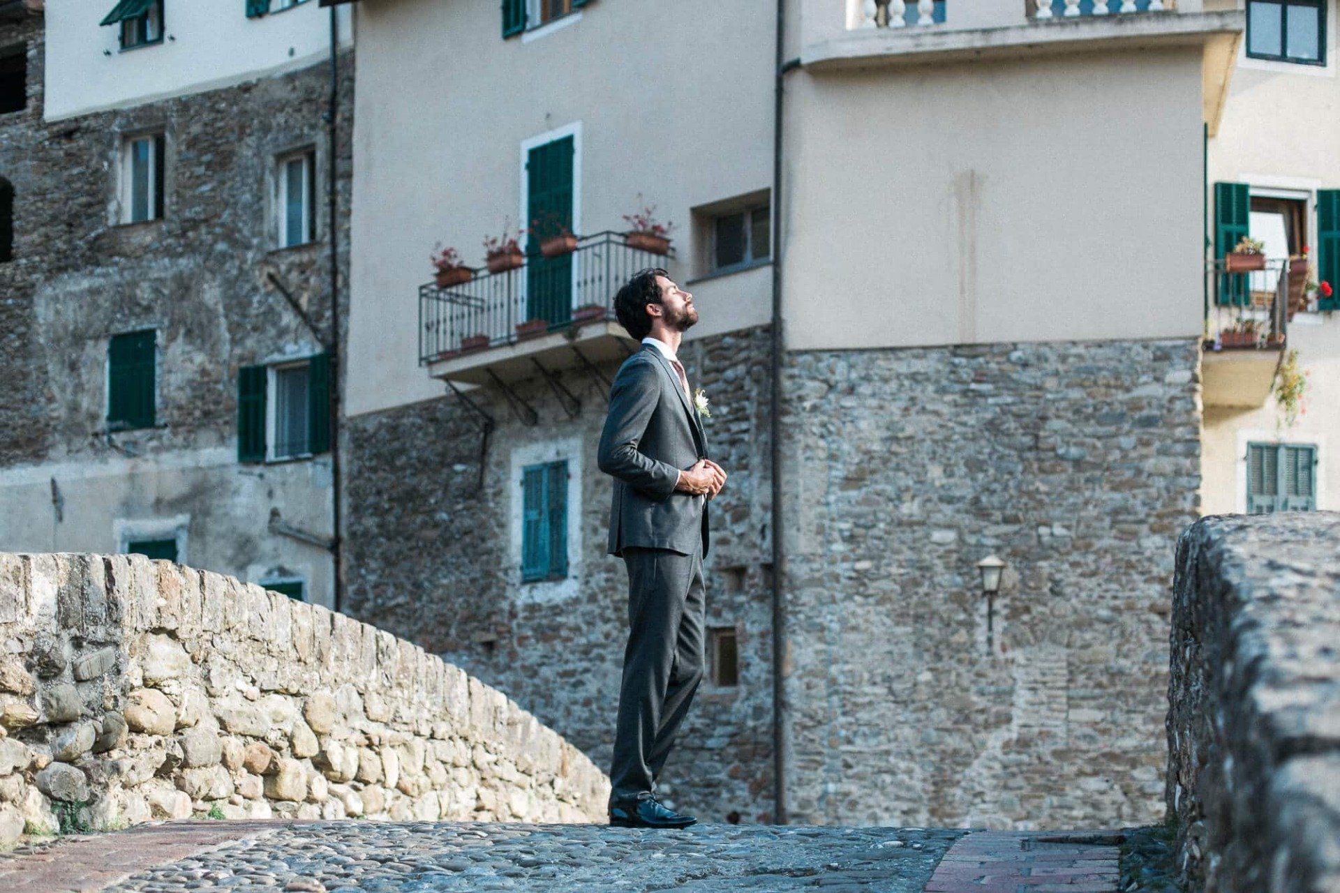 A man in a suit is standing on a stone bridge in front of a stone building.