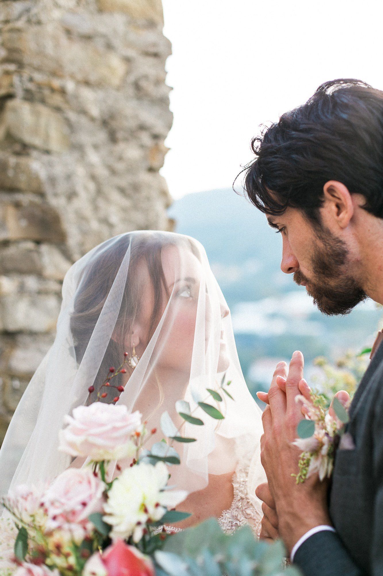 A bride and groom are holding hands and the bride is wearing a veil.