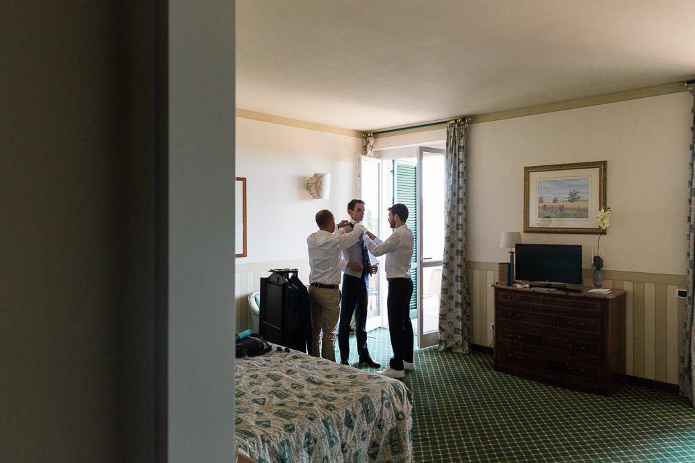 A group of men are standing in a hotel room getting ready for a wedding.