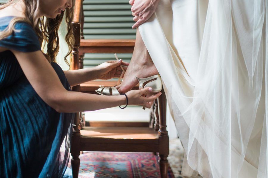 A woman in a blue dress is helping a woman in a white dress put on her shoes.
